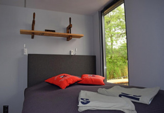 Bedroom on Houseboat Lina in Germany featuring a gray bed, shelf, open window, and red pillows.