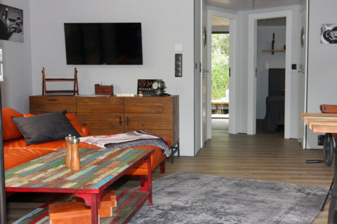 Living area on houseboat 'Lina' in Germany with orange sofa, wooden furniture, and view into bedrooms.
