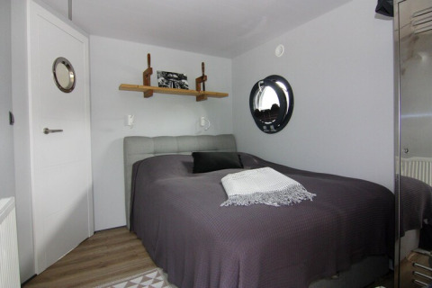 Bedroom on Houseboat «Lina» in Germany, featuring a round porthole window, bed and modern decor.