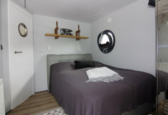 Dormitorio en la casa flotante «Lina» en Alemania, con ventana redonda, cama y decoración moderna.
