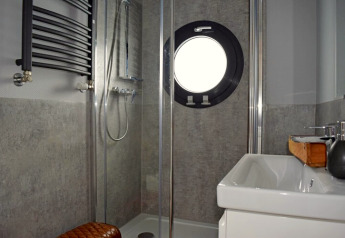 Moderne badkamer op woonboot Lina in Duitsland met douche, wastafel en een rond patrijspoortraam.