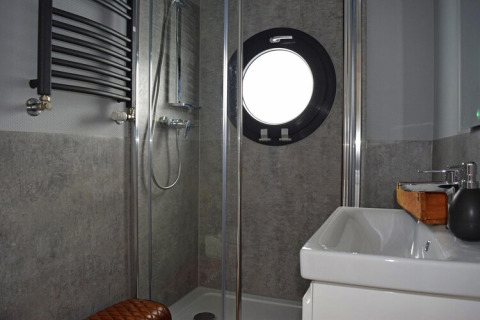 Modern bathroom on Houseboat Lina in Germany featuring a shower, sink, and round porthole window.