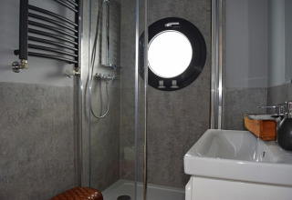Modern bathroom on Houseboat Lina in Germany featuring a shower, sink, and round porthole window.