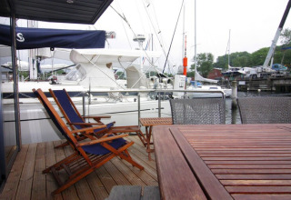 Wooden deck with chairs on Houseboat Lina in Germany, overlooking marina and docked sailboats.