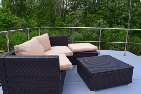 Modern outdoor lounge area with dark wicker furniture on Houseboat «Lina» in Germany, surrounded by greenery.