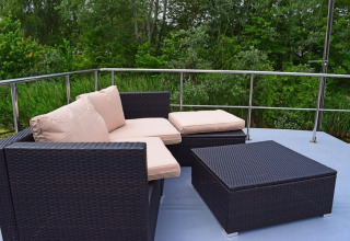 Modern outdoor lounge area with dark wicker furniture on Houseboat «Lina» in Germany, surrounded by greenery.