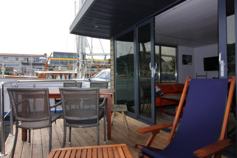 Patio on Houseboat ‘Lina’ in Germany with outdoor seating, table, and marina views through glass doors.