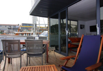 Terrasse på husbåd «Lina» i Tyskland med udendørs siddepladser, borde og udsigt over lystbådehavn.