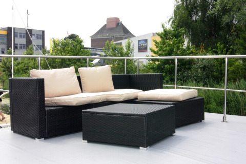 Outdoor seating area on Houseboat Lina in Germany with black wicker furniture and beige cushions on deck.