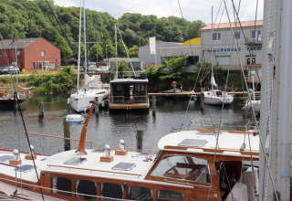 The houseboat 'Lina' is docked in a German harbor, surrounded by sailboats and lush green trees.