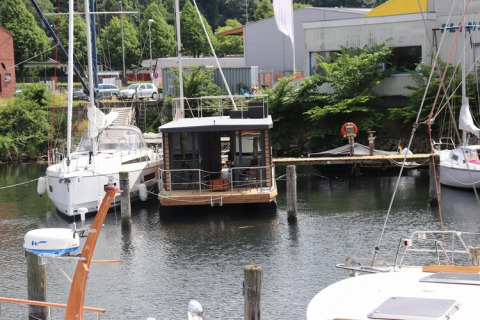 Houseboat ‘Lina’ moored at a dock in Germany, surrounded by sailboats and lush green trees in summer.