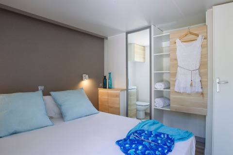 Chambre au Tamarit Park Resort 2 PATIO en Espagne avec lit double, coussins bleus et armoire ouverte.