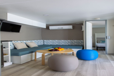 Salon moderne d’une lodge du Tamarit Park Resort 2 PATIO en Espagne avec canapé bleu, poufs et fruits.