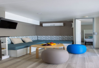 Salon moderne d’une lodge du Tamarit Park Resort 2 PATIO en Espagne avec canapé bleu, poufs et fruits.
