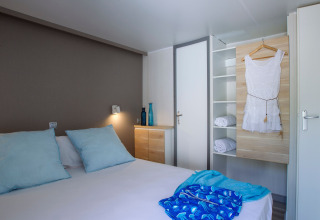 Chambre moderne au Tamarit Park Resort 2 PATIO en Espagne avec lit double, coussins bleus et armoire ouverte.