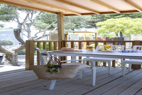 Terrasse en bois avec table à manger et chaises au Tamarit Park Resort 2 PATIO en Espagne, entourée d’arbres.