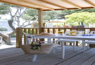 Terrasse en bois avec table à manger et chaises au Tamarit Park Resort 2 PATIO en Espagne, entourée d’arbres.