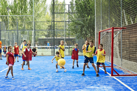 Des enfants jouent à un jeu de balle sur un terrain bleu avec des chasubles colorées à Tamarit Park Resort 2 PATIO, Espagne.