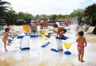 Des enfants jouent avec des jeux d’eau près de la piscine du Tamarit Park Resort 2 PATIO en Espagne, au soleil.