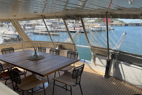 Yacht Aquamarina houseboat dining area with wooden table, chairs and marina view in the background.