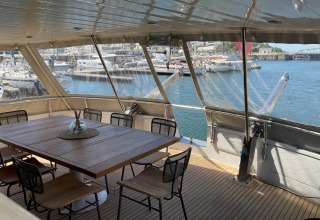 Yacht Aquamarina houseboat dining area with wooden table, chairs and marina view in the background.