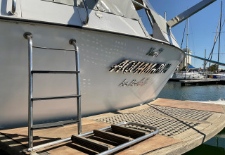 Houseboat named Yacht Aquamarina docked at the marina, ladder to a pier, name reflected on the hull.
