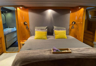 Modern bedroom on houseboat Yacht Aquamarina with double bed, wood paneling, and en-suite bathroom.