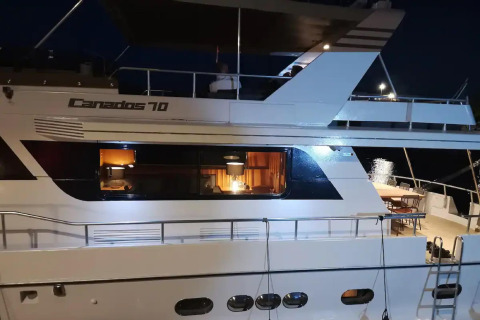 Houseboat Yacht Aquamarina docked at night, warmly lit with a view of the cozy interior through the windows.