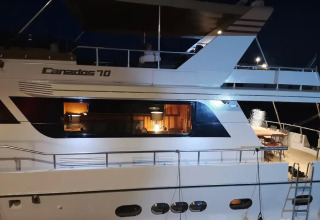Houseboat Yacht Aquamarina docked at night, warmly lit with a view of the cozy interior through the windows.