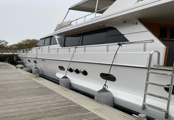 Houseboat named Yacht aquamarina docked at wooden pier, side view with fenders along the hull.