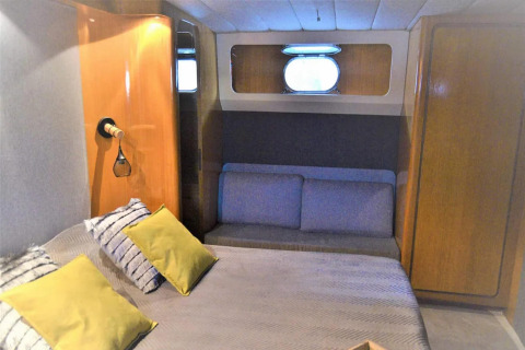Bedroom on houseboat Yacht Aquamarina with gray sofa, yellow pillows, wood cabinets and window.