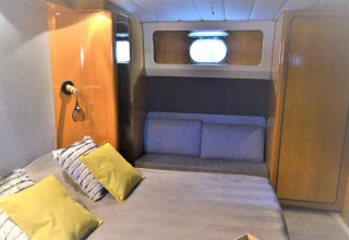 Bedroom on houseboat Yacht Aquamarina with gray sofa, yellow pillows, wood cabinets and window.