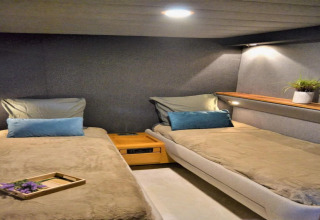 Interior view of Yacht Aquamarina houseboat featuring two single beds, cozy lighting and a potted plant.
