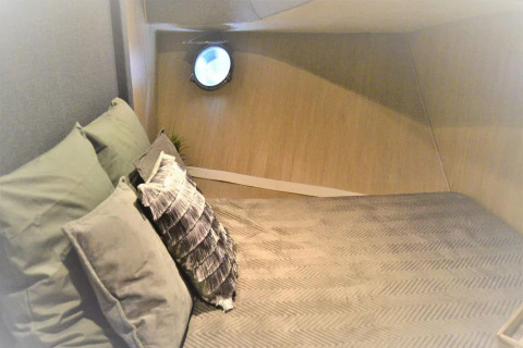 Sleeping area on houseboat Yacht Aquamarina with cozy pillows, wood paneling, and a round porthole window.