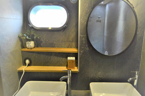 Modern houseboat bathroom on Yacht Aquamarina with two sinks, round mirror, shelves, and a plant.