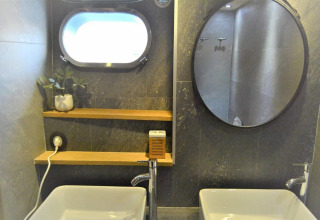 Modern houseboat bathroom on Yacht Aquamarina with two sinks, round mirror, shelves, and a plant.