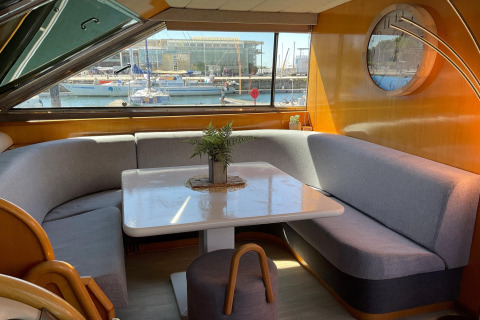 Interior lounge on Yacht Aquamarina houseboat showing dining table, grey sofas and marina view outside.