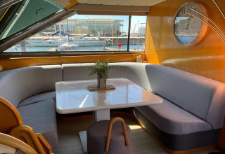Interior lounge on Yacht Aquamarina houseboat showing dining table, grey sofas and marina view outside.