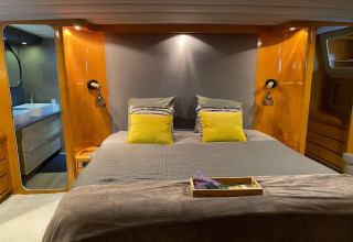 Cozy bedroom on Yacht Aquamarina houseboat with yellow pillows, wooden walls, and en suite bathroom.