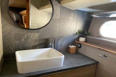 Modern bathroom on houseboat Yacht Aquamarina with rectangular sink, circular mirror, and porthole window.