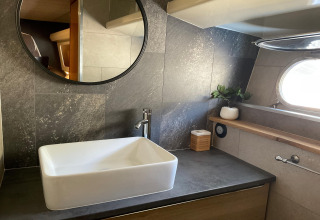 Modern bathroom on houseboat Yacht Aquamarina with rectangular sink, circular mirror, and porthole window.