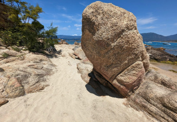 Großer Felsen am Sandstrand bei Résidence U Livanti Belvédère Campomoro, mit Meer und Bergen im Hintergrund.