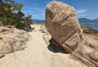 Gran roca en una playa de arena en Résidence U Livanti Belvédère Campomoro, Francia, con el mar y barcos.