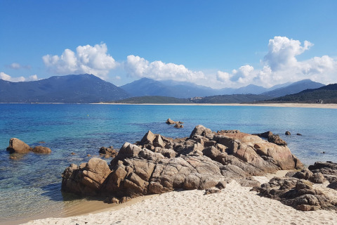 Playa de arena con rocas y mar azul en Résidence U Livanti Belvédère Campomoro, Francia.