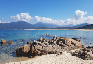 Playa de arena con rocas y mar azul en Résidence U Livanti Belvédère Campomoro, Francia.