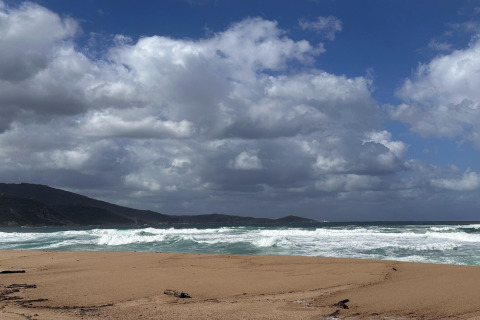 Playa de arena, olas y montañas bajo nubes dramáticas en Résidence U Livanti Belvédère Campomoro, Francia.