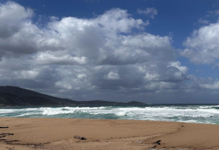 Playa de arena, olas y montañas bajo nubes dramáticas en Résidence U Livanti Belvédère Campomoro, Francia.