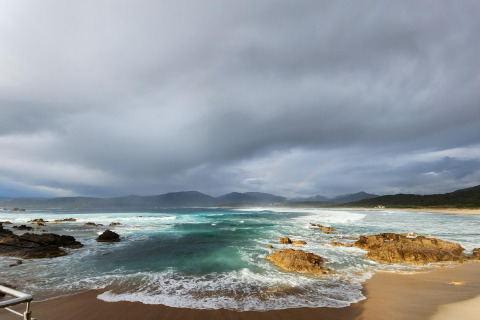 Playa rocosa con olas y cielo nublado en Résidence U Livanti Belvédère Campomoro en Francia.