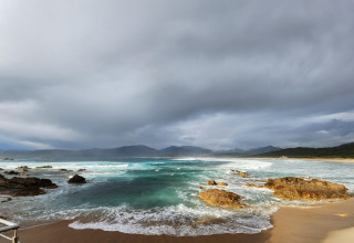 Playa rocosa con olas y cielo nublado en Résidence U Livanti Belvédère Campomoro en Francia.