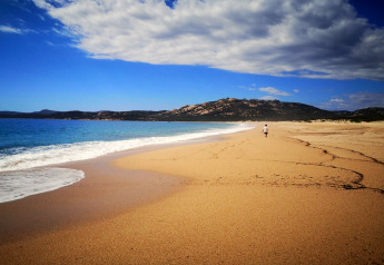 Einzelne Person spaziert am leeren Strand bei Résidence U Livanti Belvédère Campomoro in Frankreich mit Hügeln im Hintergrund.